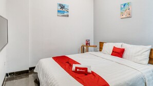 A hotel room with a bed, a red towel, a small table with a book, and two paintings on the walls.