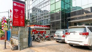 A RedDoorz building with a signboard listing amenities like free WiFi, mineral water, television, and bathroom. There are parked cars and motorcycles in front.