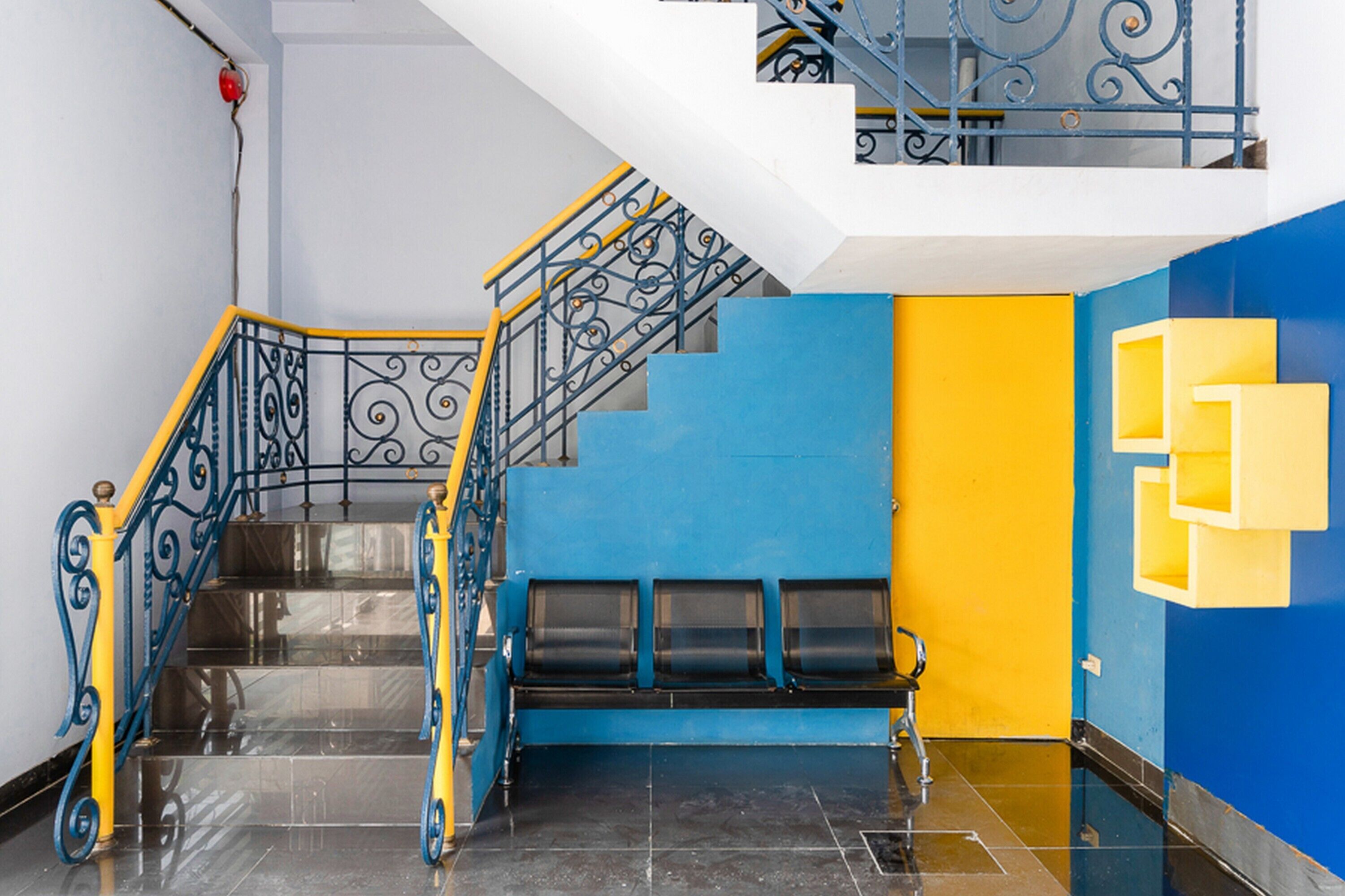 A staircase with black and yellow railings, a blue wall, and a yellow geometric wall decoration.