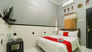 Habitación de hotel con una cama, una mesita de noche pequeña, aire acondicionado en la pared, un reloj y una puerta.
