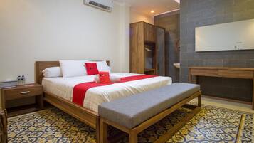 Una habitación de hotel con cama, una banca, mesita de noche, armario y una pequeña mesa.