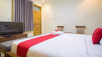 Habitación de hotel con cama, televisor sobre una mesita de noche de madera, puerta de madera y ventana con cortinas.