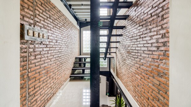 A corridor with brick walls, a metal staircase, and a ceiling with exposed beams.