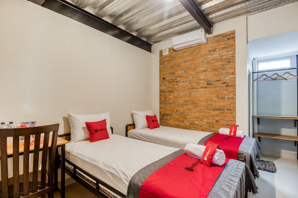 Une chambre d’hôtel avec deux lits, une chaise en bois, un mur en briques et un plafond en métal.