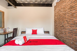 Habitación de hotel con pared de ladrillo, estructura de cama de madera, cubrecama blanco y manta roja con la marca RedDoorz.