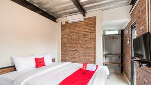A hotel room with a bed, a brick wall, a television, and a coat rack.