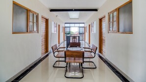 A long, narrow hallway with a central table and chairs, flanked by windows with wooden frames.