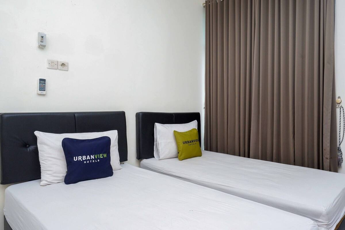 Ein Hotelzimmer mit zwei Betten, jeweils mit Kissen, einer Steckdose und einem Telefon.