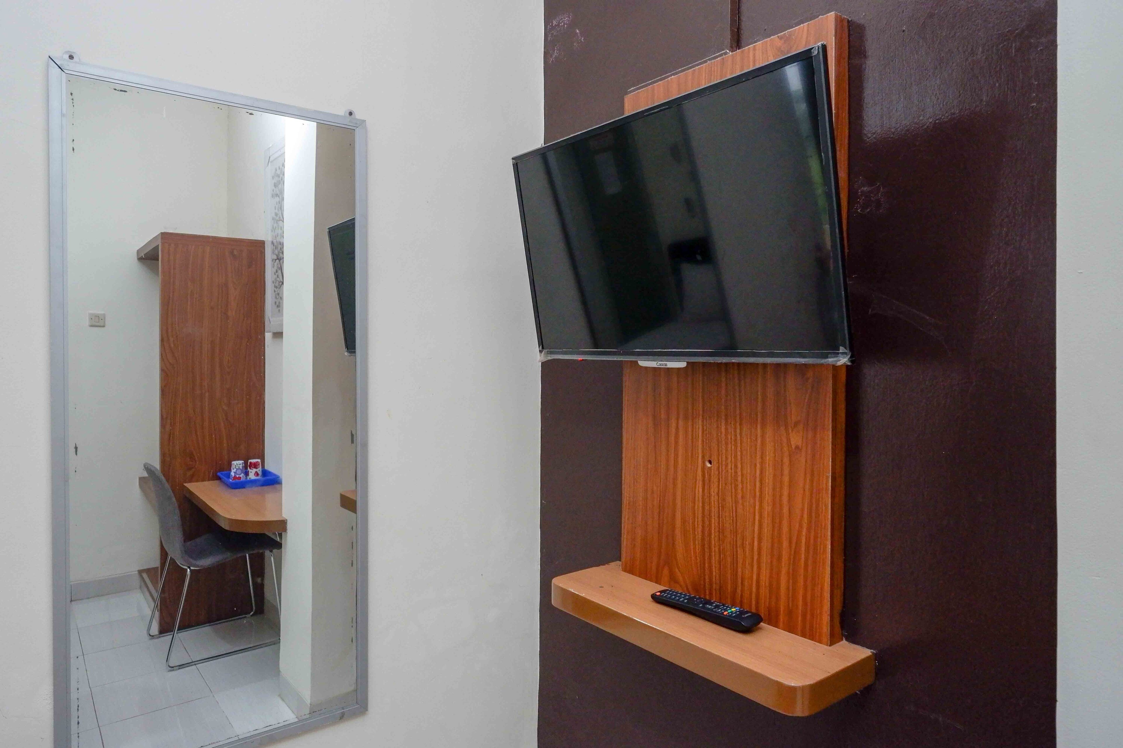 A room with a TV mounted on a wooden shelf, a chair, and a small table with a tray.