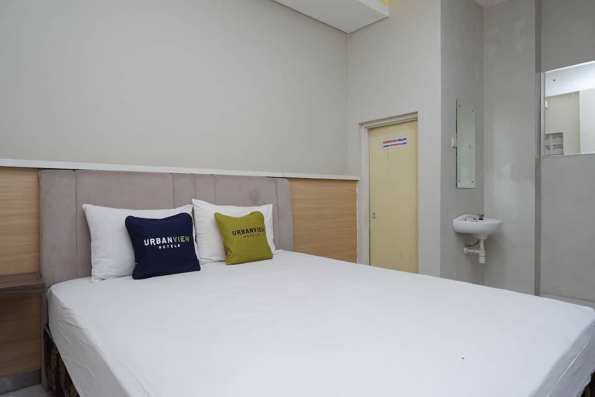 Ein Hotelzimmer mit einem Bett, zwei Kissen, einem Nachttisch, einem Spiegel und einem Waschbecken.