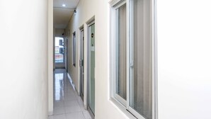 A narrow hallway with doors and windows, leading to a bright room. - Urbanview Hotel Double Tree Purwokerto (Purwokerto)