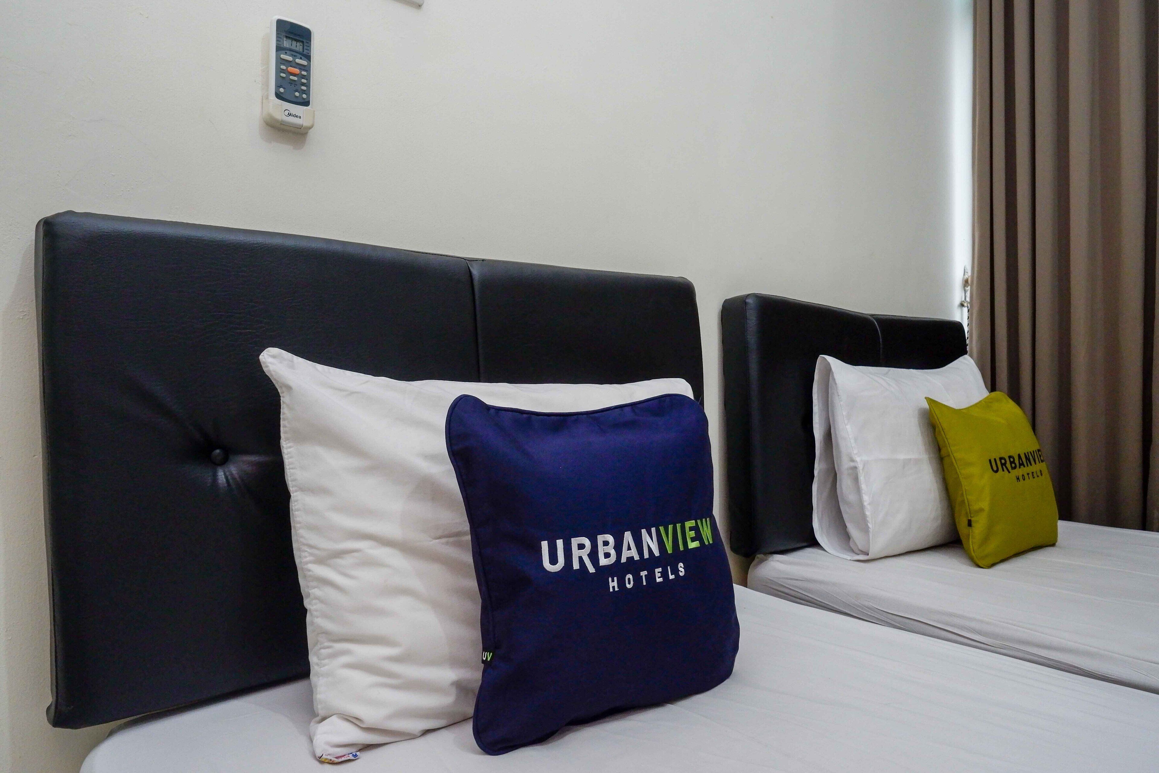 A hotel room with a black headboard, two beds, and pillows with "URBANVIEW HOTELS" branding.