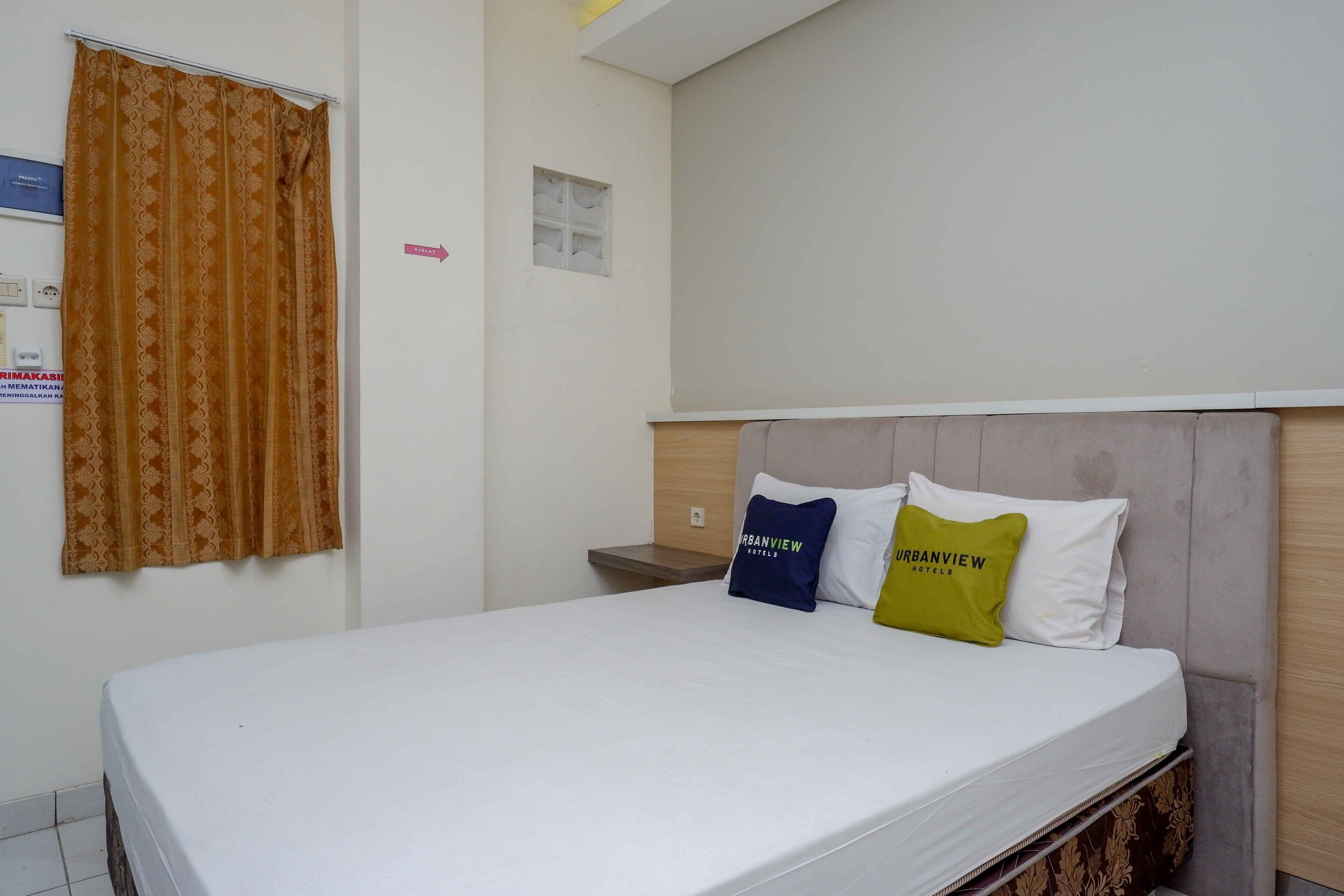 A hotel room with a bed, two pillows, a nightstand, and a window with curtains.