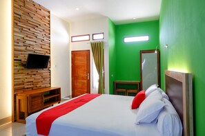 A bedroom with a bed, a wooden headboard, a TV mounted on the wall, and a green wall. - RedDoorz near Taman Makam Pahlawan Tatura (Palu)