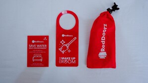 Três itens da marca RedDoorz: um cartão, um chaveiro e uma sacola com cordão, todos incentivando a conservação da água.