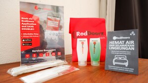 Um display promocional da RedDoorz com um anúncio de aplicativo móvel, uma sacola RedDoorz e um folheto sobre uma mesa de madeira.