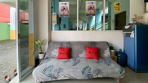 Una habitación con sofá cama, dos almohadas rojas, una planta en maceta y un dispensador de agua.
