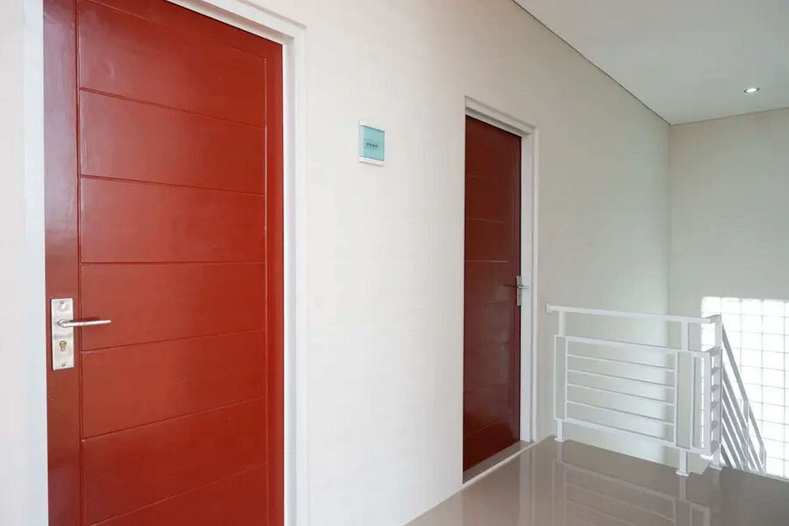 Un pasillo con dos puertas rojas, una barandilla blanca y una pequeña señal en la pared.