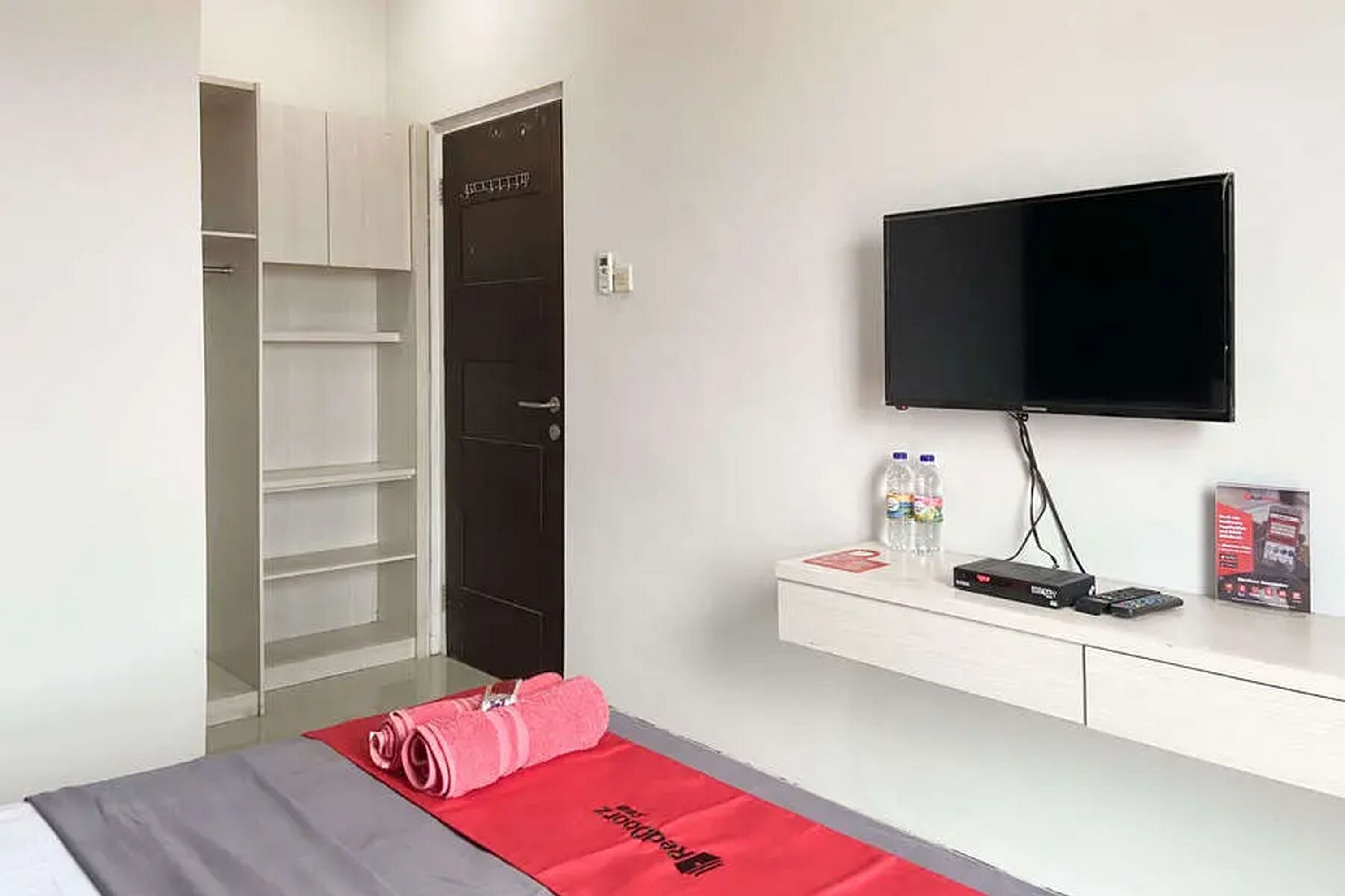 A hotel room with a bed, a TV mounted on the wall, a minibar, and a door leading to a closet.