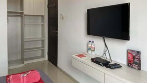 Habitación de hotel con televisor montado en la pared, minibar, una toalla roja y armario.