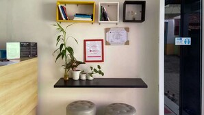 Zona de recepción con un mostrador de madera, una planta en maceta, un certificado enmarcado y dos cubos de basura.