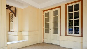 A room with a tiled floor, a window with a view of greenery, and a door with frosted glass panels.