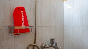 A shower area with a RedDoorz towel rack and a showerhead.