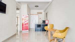 A hotel lobby with a reception desk, two yellow chairs, a white wardrobe, and a red promotional banner. - RedDoorz near UNTAG Surabaya (Surabaya)