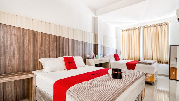 A modern hotel room with a wooden headboard, a large bed with red accents, a bedside table, and a mirror. - RedDoorz near UNTAG Surabaya (Surabaya)
