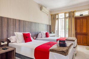 A hotel room with two beds, a wooden headboard, a window with curtains, and a door.