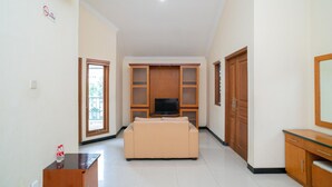 A living room with a beige sofa, a TV on a stand, wooden cabinets, and a glass cabinet. - RedDoorz near Rumah Sakit Baptis Kediri (Kediri)