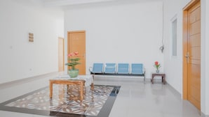 A clean, modern lobby with a reception desk, a waiting area with blue chairs, and a wooden door. - RedDoorz Syariah near Pahoman Stadium Lampung (Bandar Lampung)