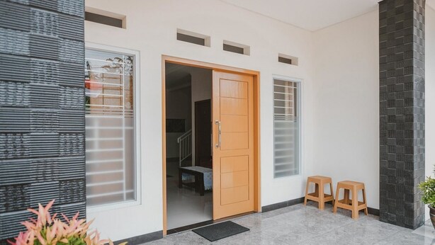 A modern entrance with a wooden door, two stools, and a potted plant. - RedDoorz Syariah near Pahoman Stadium Lampung (Bandar Lampung)