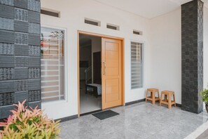 A modern entrance with a wooden door, two stools, and a potted plant.