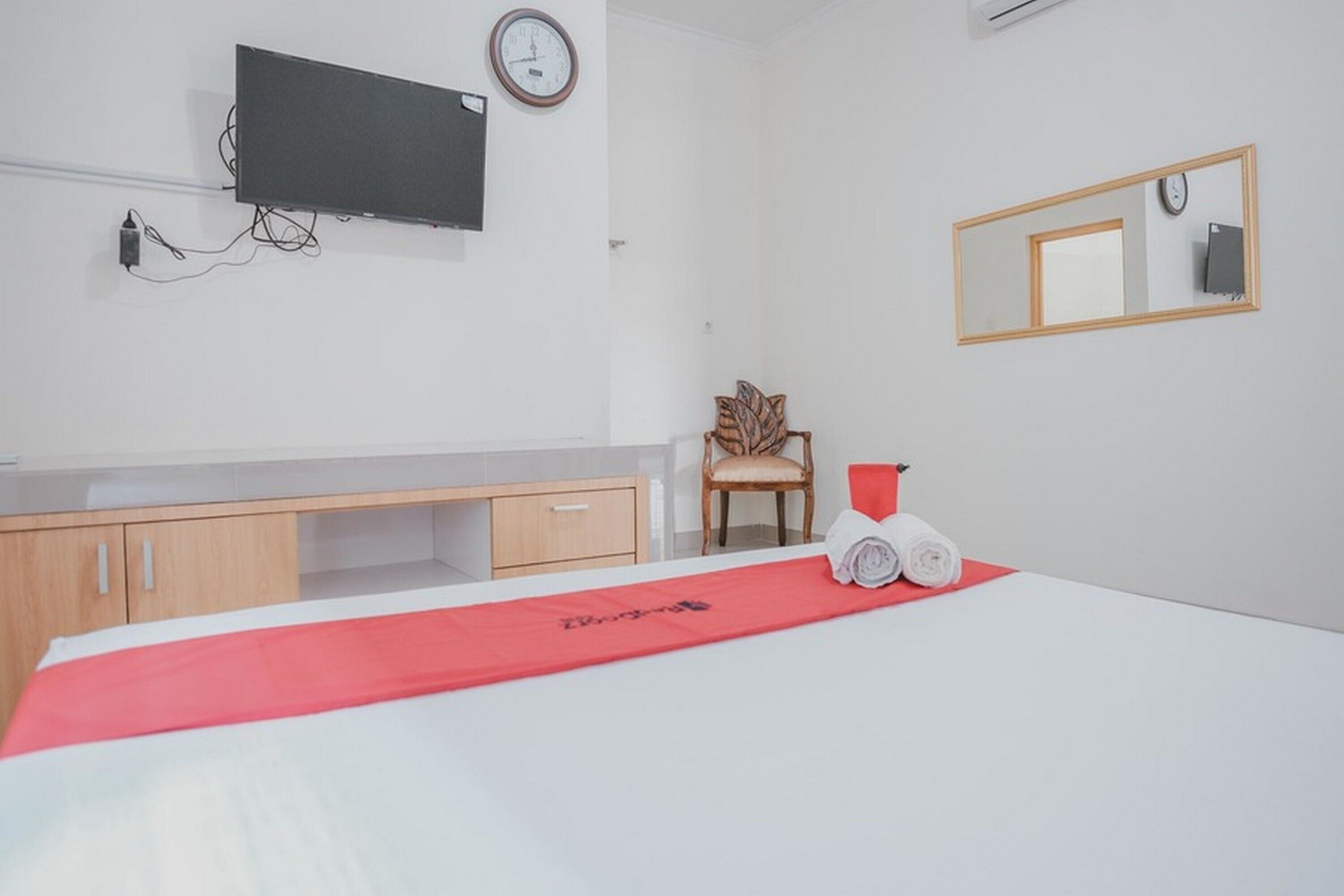 Habitación de hotel con una cama, un escritorio de madera, una silla, un televisor, un reloj y un espejo.