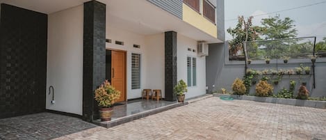 A modern two-story house with a paved courtyard, a wooden door, and potted plants.