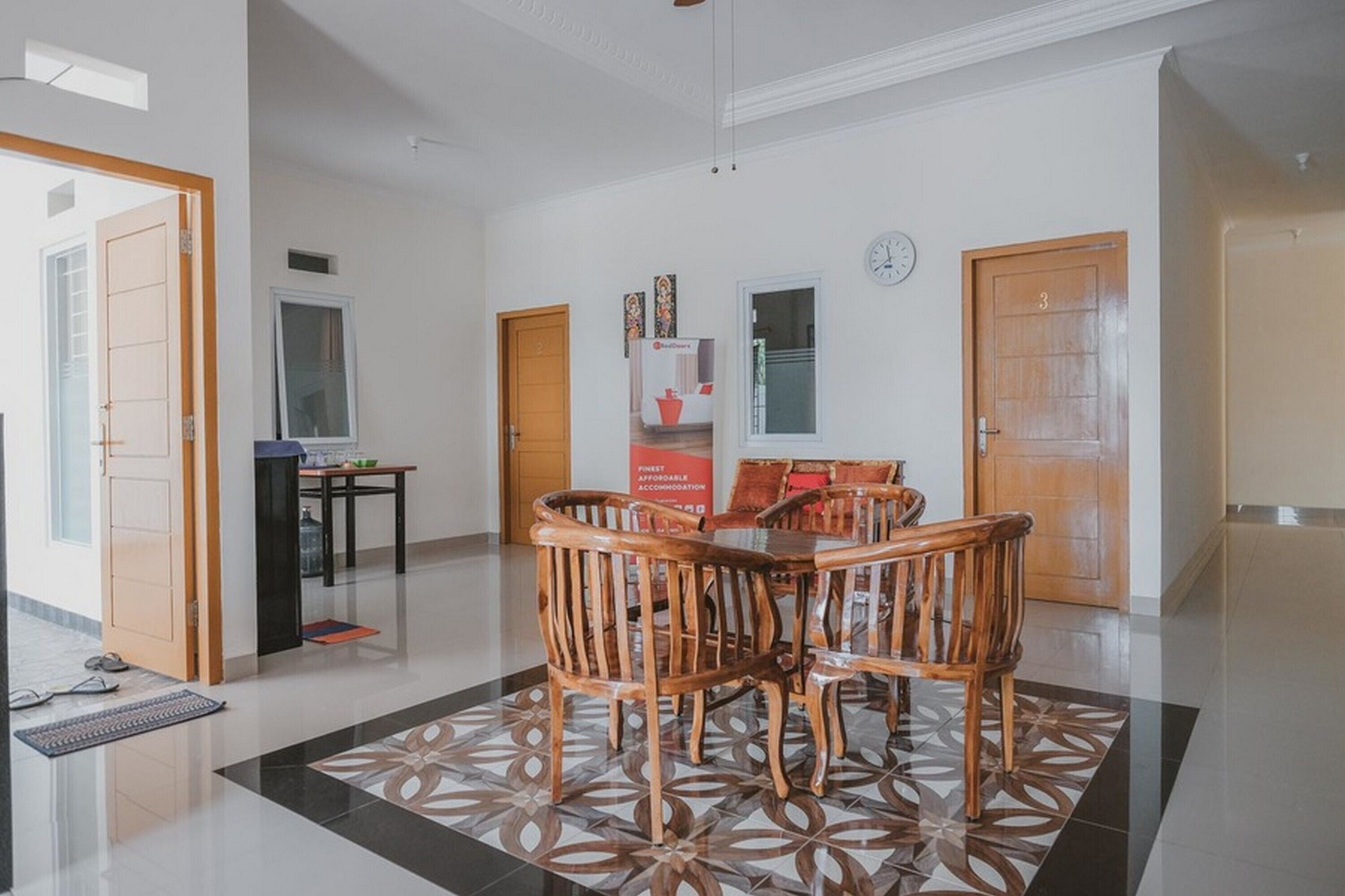 A spacious lobby with a wooden dining table and chairs, a reception desk, and a clock on the wall.