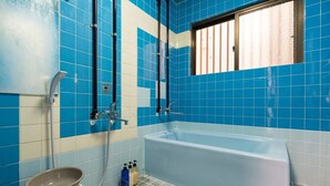 A bathroom with a bathtub, blue and white tiles, a window, and a showerhead. - Naha Tomarin House (Naha)