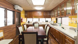 A kitchen with wooden cabinets, a dining table, and chairs. There is a window on the left side, a fire extinguisher, and a microwave on the counter. - Naha Tomarin House (Naha)