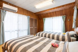 A room with two beds, wooden paneling, an air conditioning unit, and a window with curtains. - Naha Tomarin House (Naha)