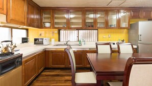 A kitchen with wooden cabinets, a microwave, a stove, a sink, and a dining table with chairs. - Naha Tomarin House (Naha)