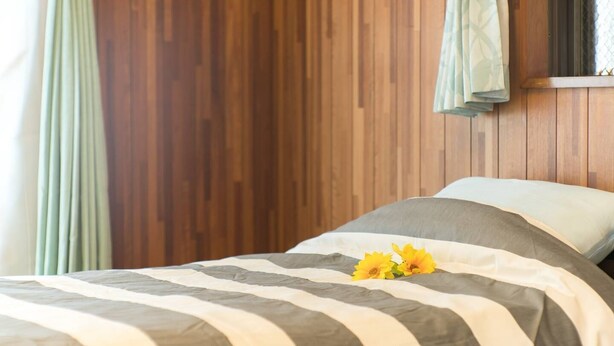 A bed with striped bedding and a single yellow flower. - Naha Tomarin House (Naha)