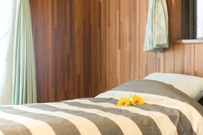 A bed with striped bedding and a single yellow flower. - Naha Tomarin House (Naha)