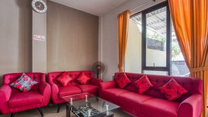 A living room with two red sofas, a glass coffee table, and a wall clock. - RedDoorz Syariah near Airlangga University Campus B (Surabaya)