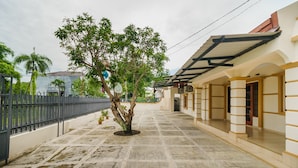 A covered outdoor area with a stone floor, a tree, and a building with a white facade and yellow trim.