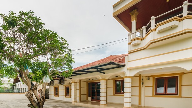 A building with a covered entrance, a tree in front, and a balcony with railings.