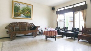 A room with a wooden bench, a table with a patterned tablecloth, and a painting of a river scene on the wall. - RedDoorz Syariah @ Jalan Gajah Mada (Jember)