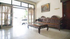 A spacious room with a glass door leading outside, a wooden bench, and a framed picture on the wall. - RedDoorz Syariah @ Jalan Gajah Mada (Jember)