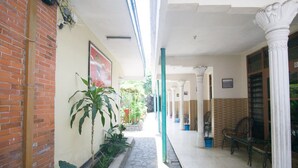 A covered corridor with brick walls, potted plants, and white columns. - RedDoorz Syariah @ Jalan Gajah Mada (Jember)