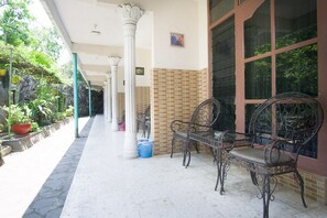 A covered outdoor area with a tiled floor, white columns, and a brick wall. There are metal chairs and a table, and potted plants are visible. - RedDoorz Syariah @ Jalan Gajah Mada (Jember)